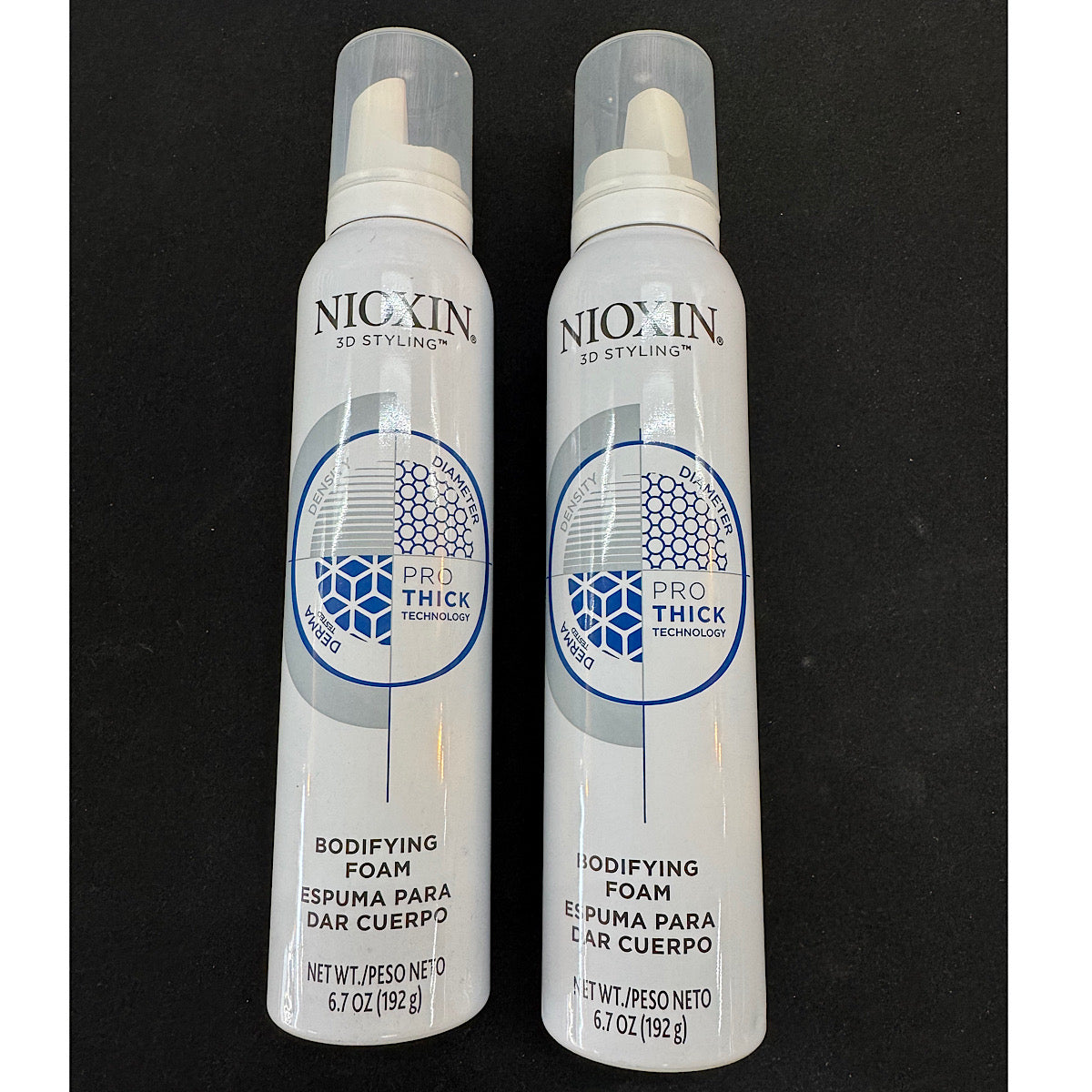 Two white Nixxin 3D Styling Pro Thick Technology Bodifying Foam spray cans standing side-by-side on a black background.
