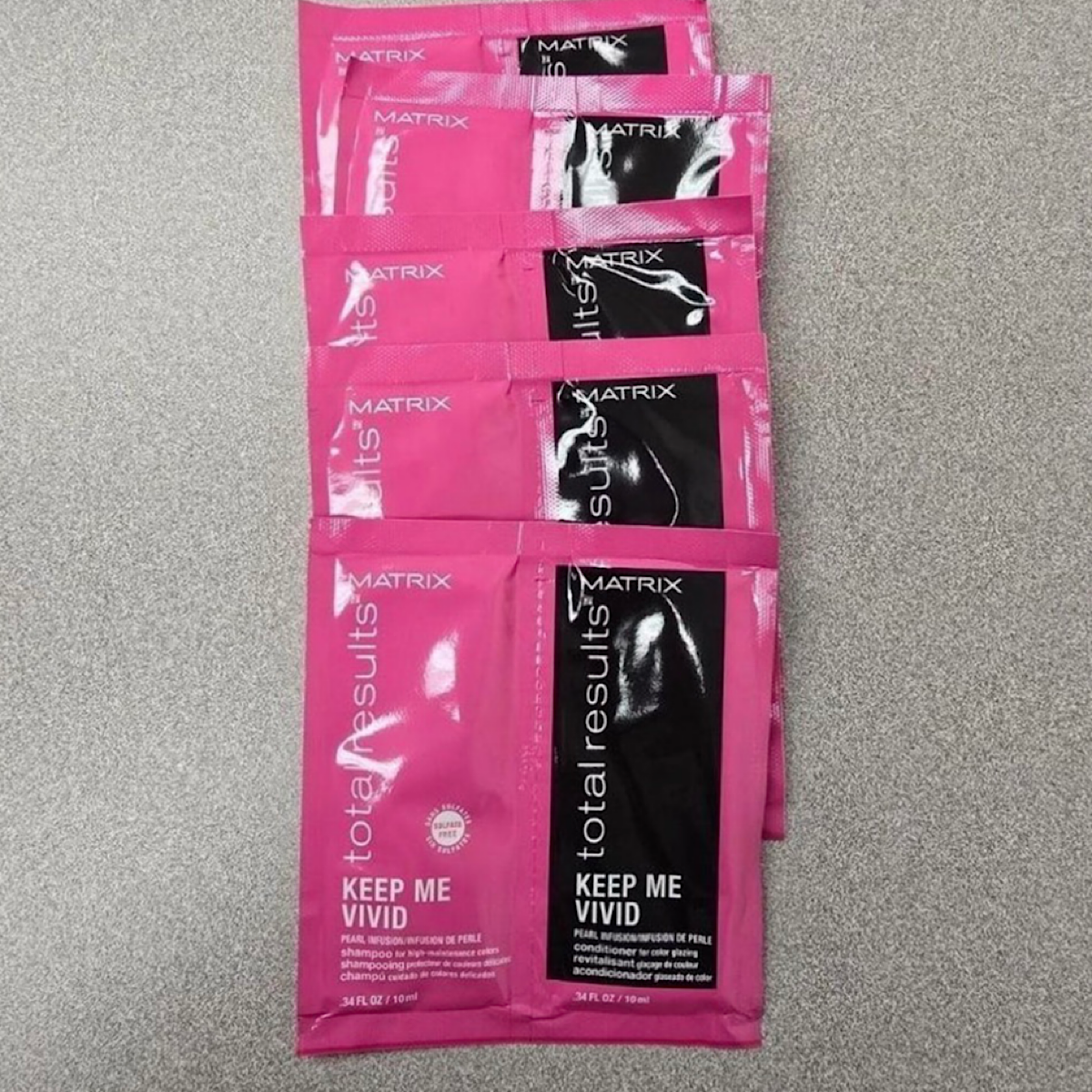 Six pink and black Matrix Total Results Keep Me Vivid hair extension swab packets arranged vertically on a gray textured surface.