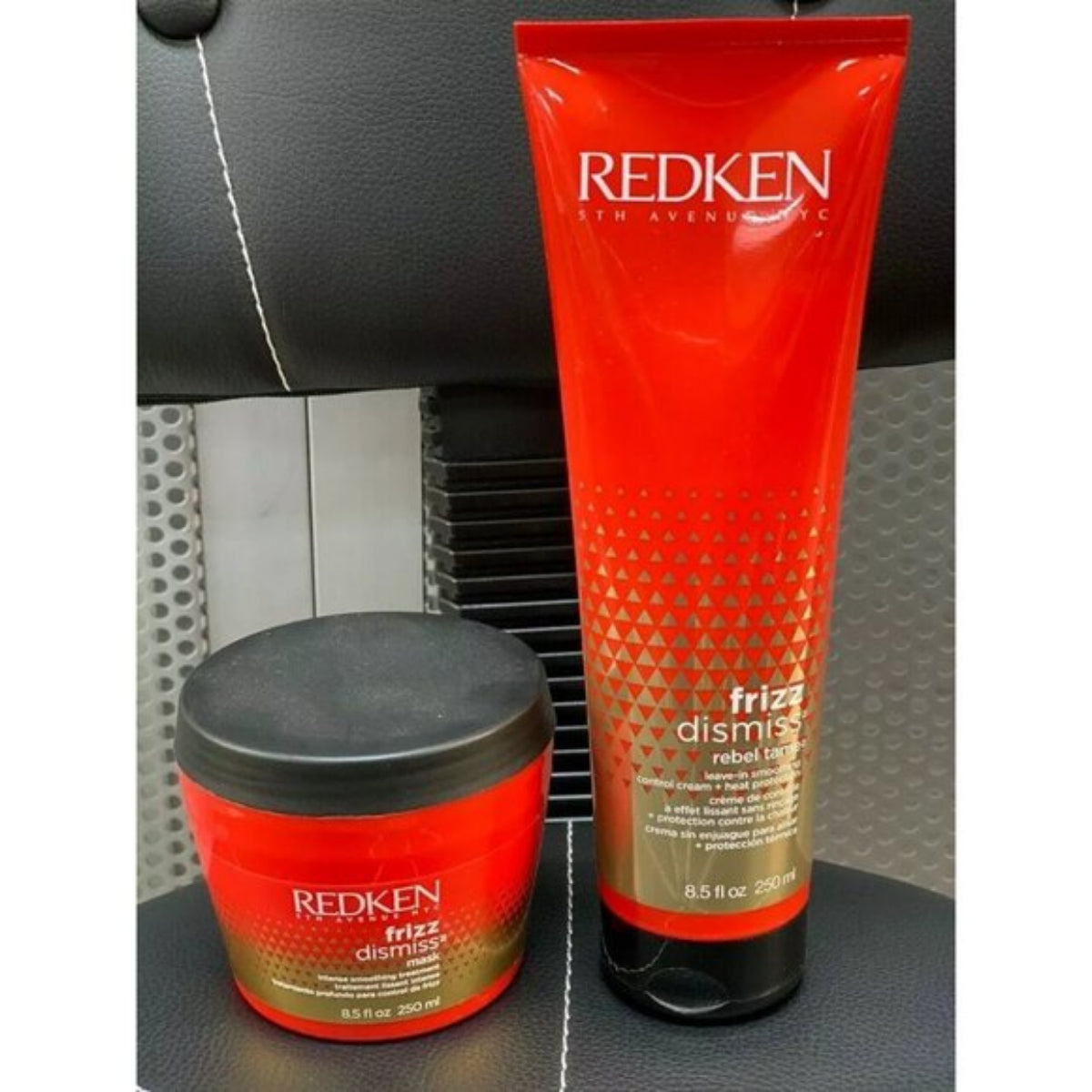 REDKEN Frizz Dismiss Rebel Hair Care set, featuring a 200ml red squeeze tube and a 200g red jar with a black lid, displayed on a black textured leather surface.