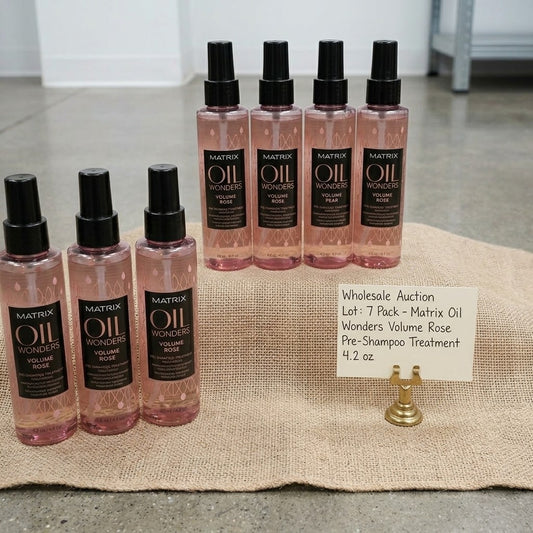 7 bottles of Matrix Oil Wonders Volume Rose pre-shampoo treatment arranged on a burlap cloth, with a handwritten price tag card in front. The bottles are pink with black caps and black labels.
